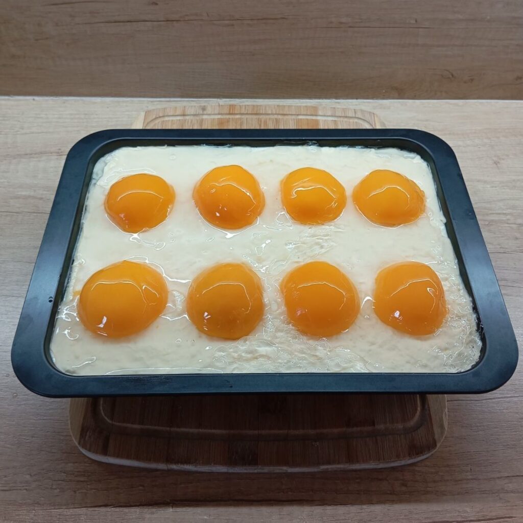 Freshly baked peach custard cake in a rectangular pan topped with peach halves and glossy glaze.