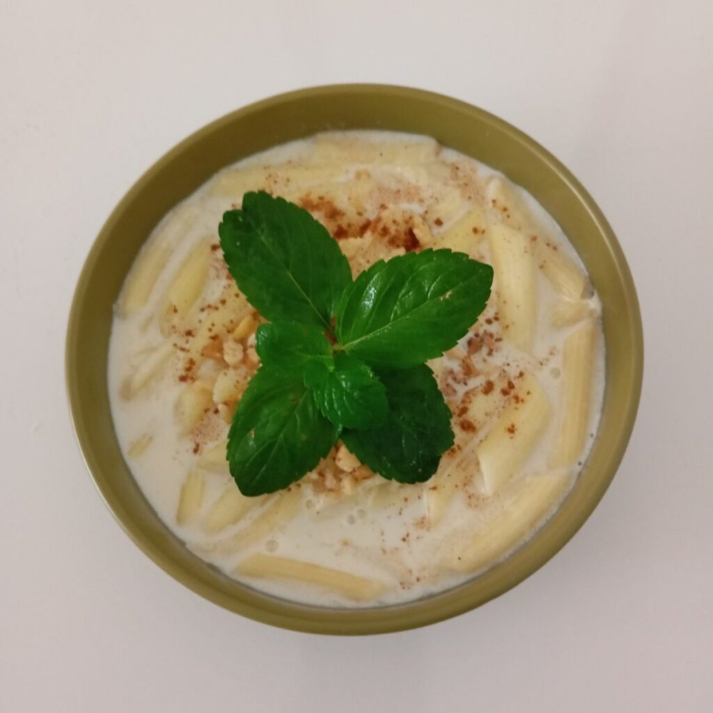 Sweet Milk Pasta Delight served in a green bowl with cinnamon, chopped walnuts, and fresh mint on top.
