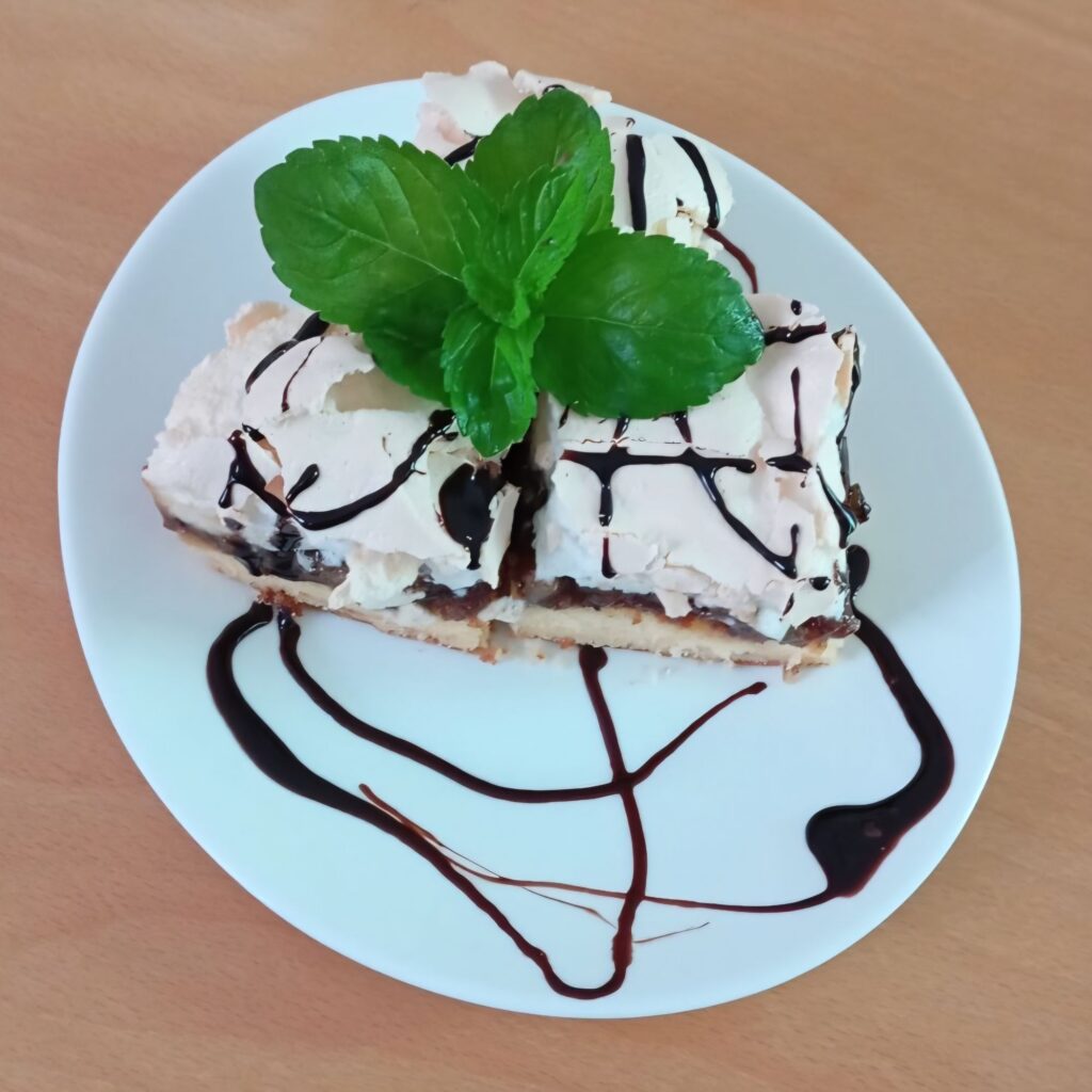 Served portion of Fig Walnut Marshmallow Cake with three sliced squares topped with liquid chocolate and decorated with fresh mint leaves on a flat plate.