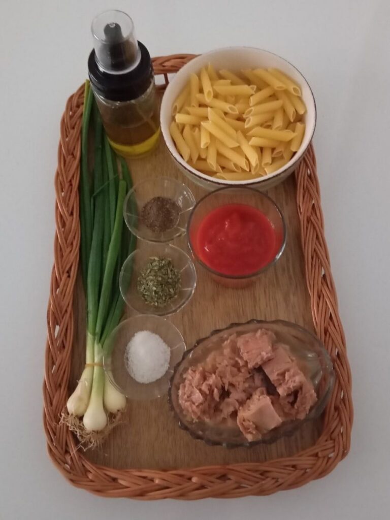 Macaroni, canned tuna, tomato puree, young onions, oregano, black pepper, salt, and oil arranged on a table.