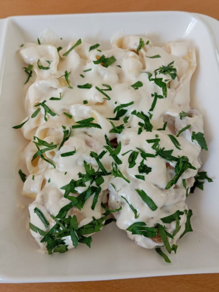 Close view of creamy cheese chicken tagliatelle with tender chicken pieces, smooth sauce, and fresh parsley on top.