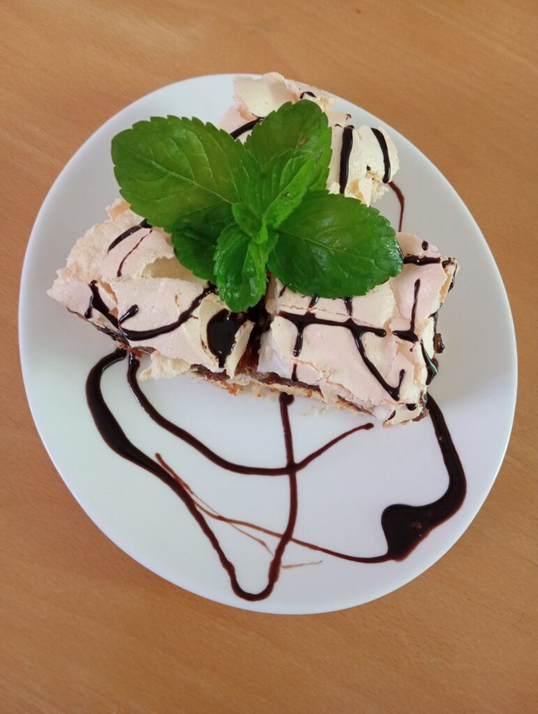 Three sliced pieces of Fig Walnut Marshmallow Cake topped with chocolate drizzle and decorated with fresh mint leaves on a flat serving plate.