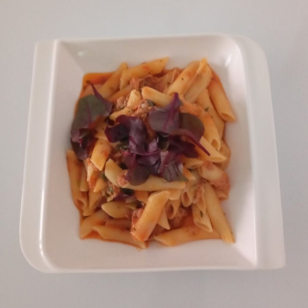Creamy Tuna Pasta Delight served in a deep plate with tuna, macaroni, tomato sauce, and fresh mixed microgreens on top.