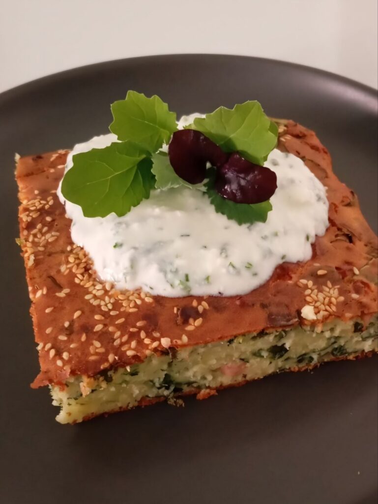 Close view of sliced savory cheese ham loaf topped with creamy chive spread and fresh microgreens on a serving plate.