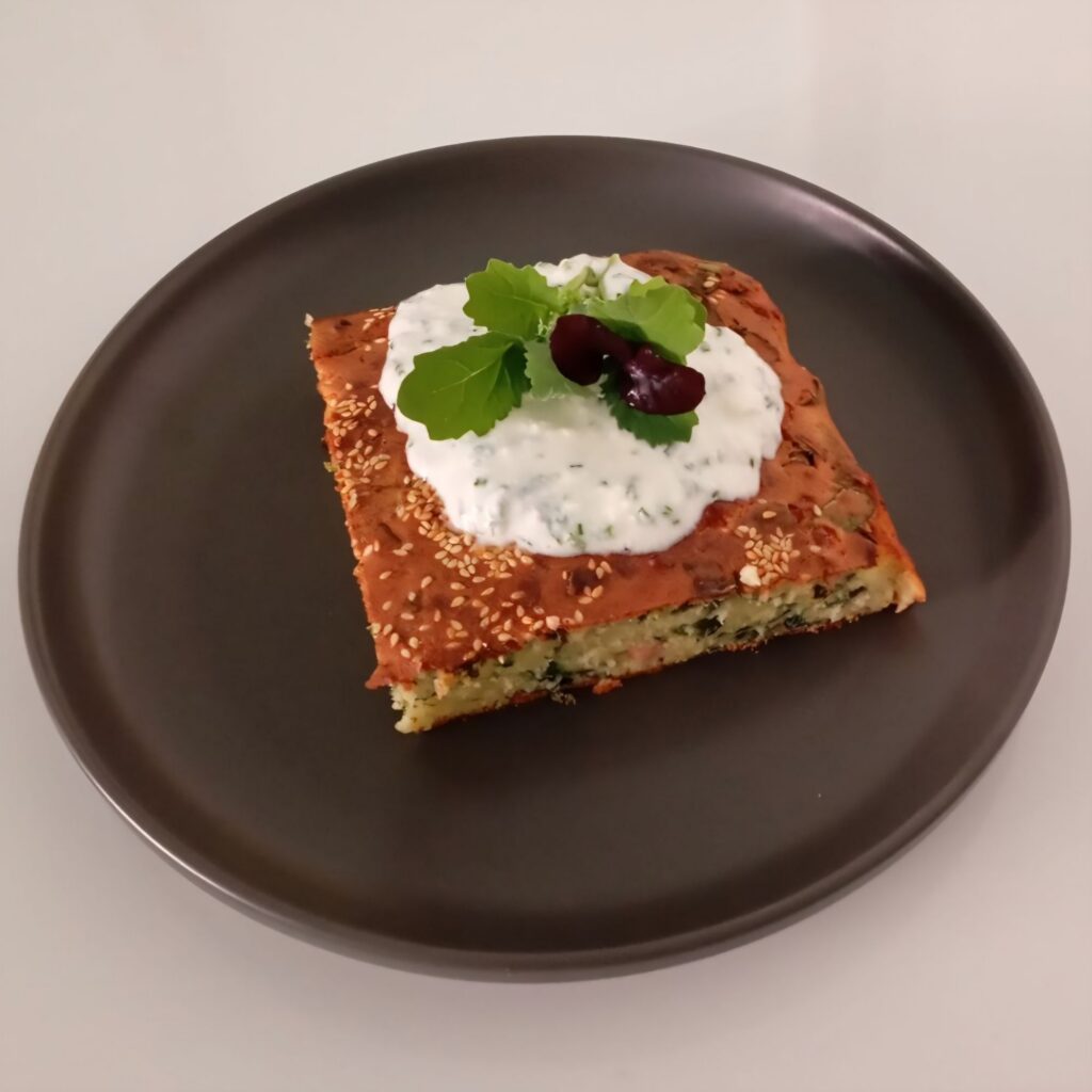 Served piece of Savory Cheese Ham Loaf topped with creamy chive spread and decorated with fresh microgreens on a plate.