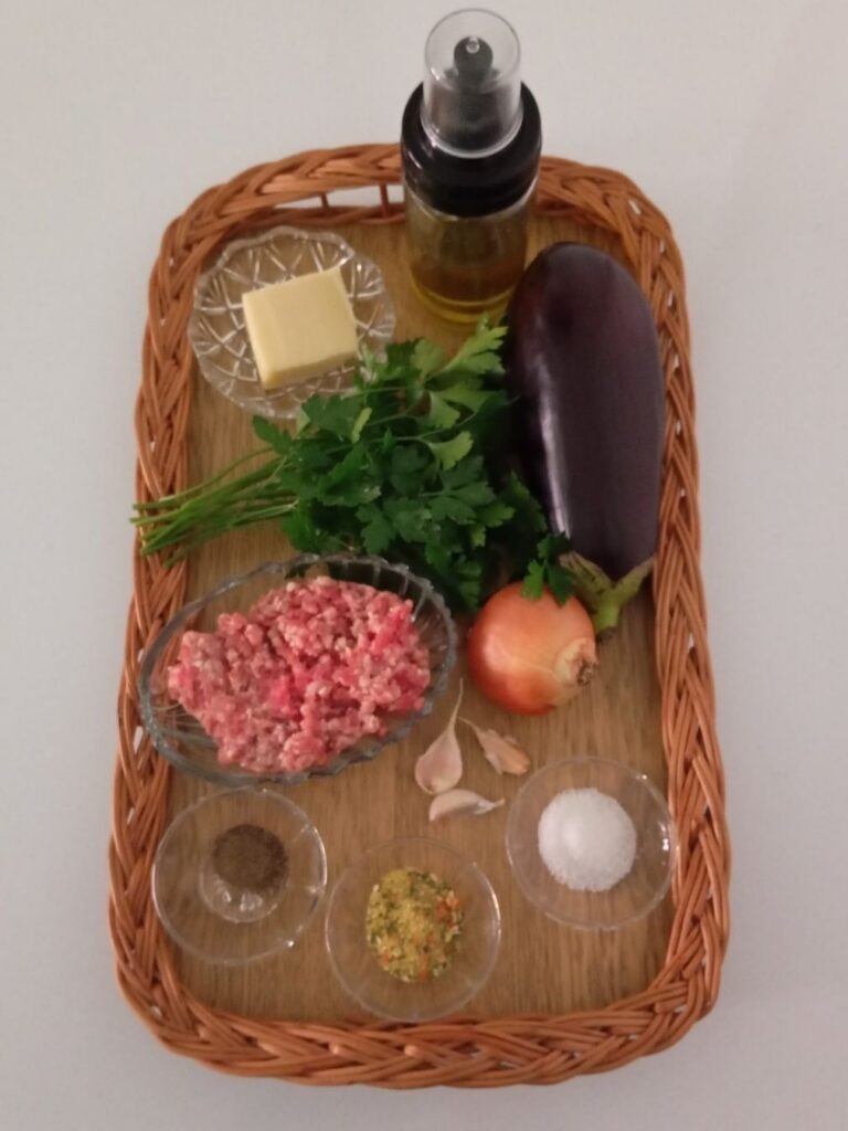 Fresh ingredients for stuffed eggplant with minced meat and cheese arranged on a kitchen table with eggplant, onion, garlic, parsley, and cheese.