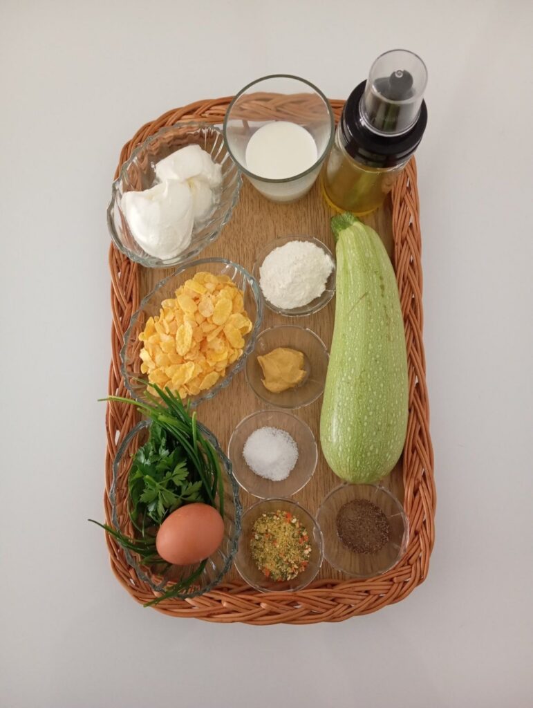 Fresh zucchini, eggs, flour, cornflakes, sour cream, mustard, and herbs prepared for crunchy fried zucchini strips recipe.