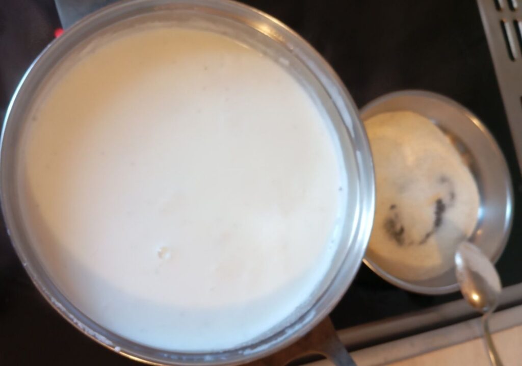 Pasta cooking in milk inside a deep pot while semolina toasts in a pan until lightly golden.