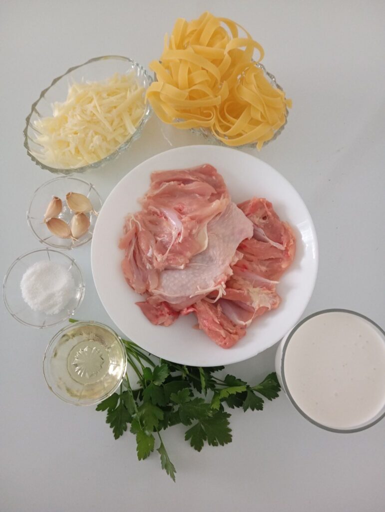 Chicken, cooking cream, grated cheese, garlic, tagliatelle, oil, parsley, and salt arranged for creamy chicken pasta preparation.