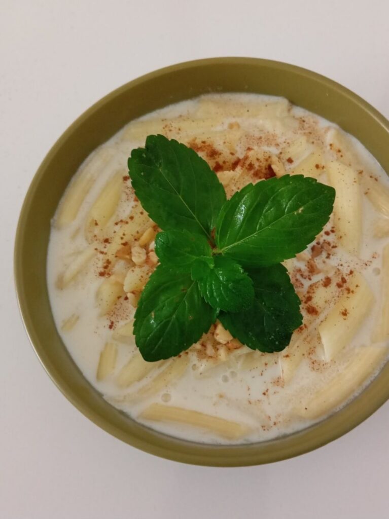 Close-up of sweet milk pasta served in a bowl with cinnamon, chopped walnuts, and fresh mint on top.